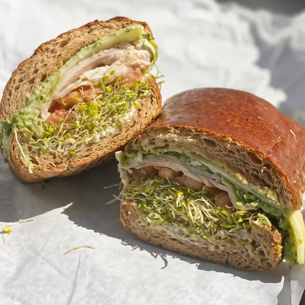 A Picnicky's Sandwich Shop sandwich, cut in half, filled with meat, sprouts, and avocado spread.