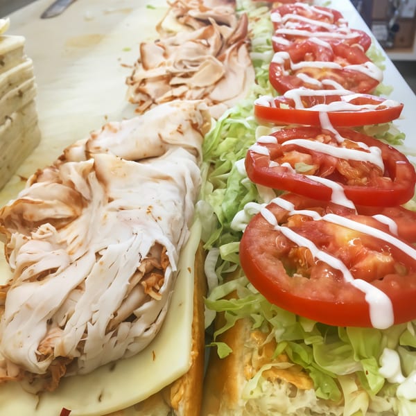 Picnicky's sandwich being assembled with turkey, cheese, lettuce, and tomatoes drizzled with dressing.