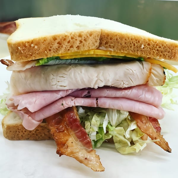 A towering Picnicky's sandwich with turkey, ham, bacon, cheese, and lettuce on white bread.