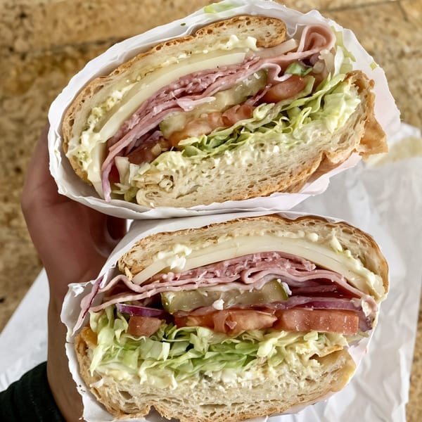 A hand holds a large Picnicky's sandwich, cut in half, revealing layers of meat, cheese, and vegetables.