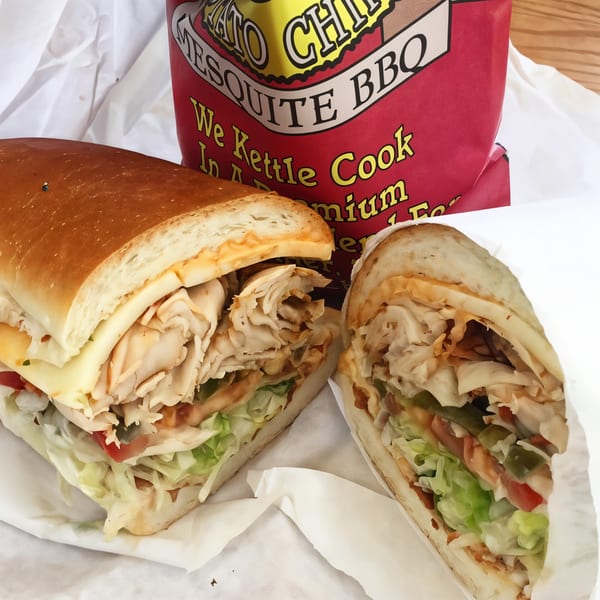 A large Picnicky's turkey sandwich, cut in half, with lettuce, tomato, and cheese, next to a bag of chips.
